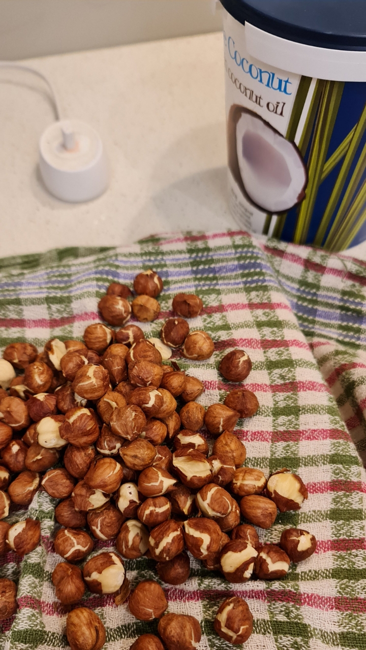 Hazelnuts spread on a tea towel next to a tub of coconut oil
