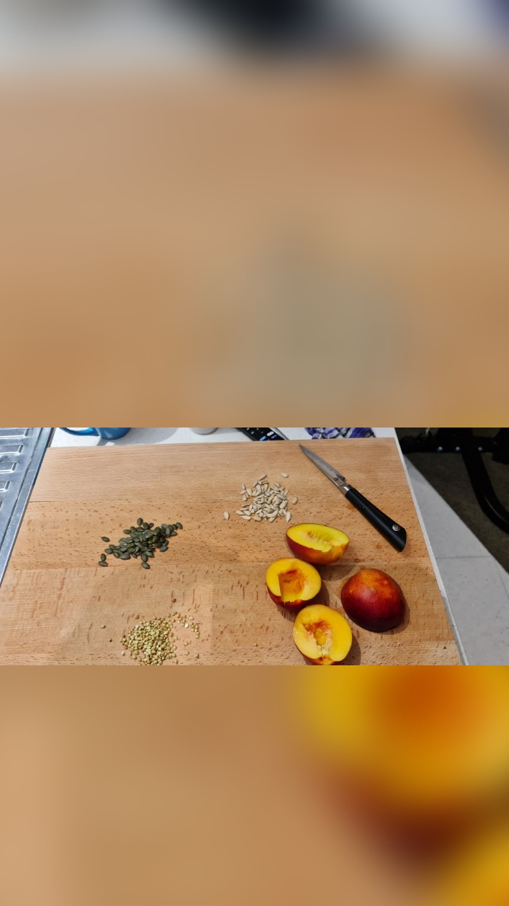 Prep board with piles of pumpkin, sunflower and buckwheat seeds beside halved nectarines