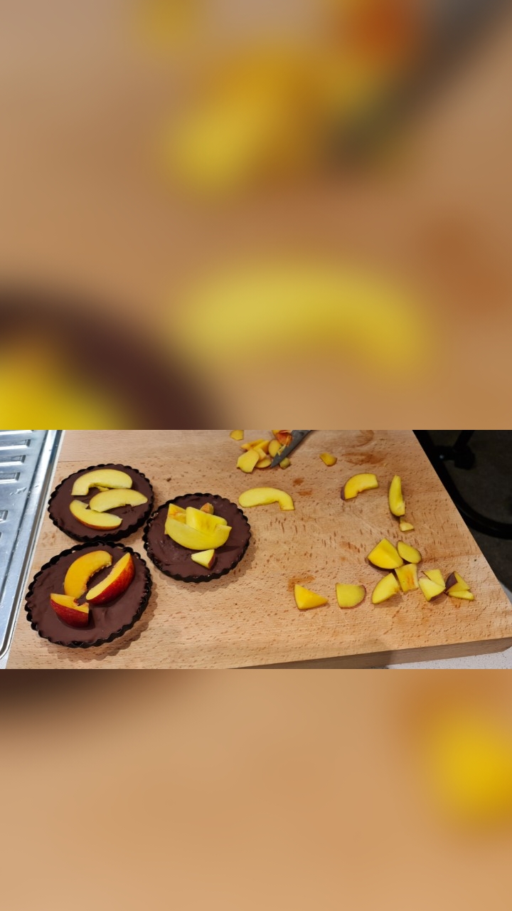 Three chocolate tart bases being topped with sliced nectarine