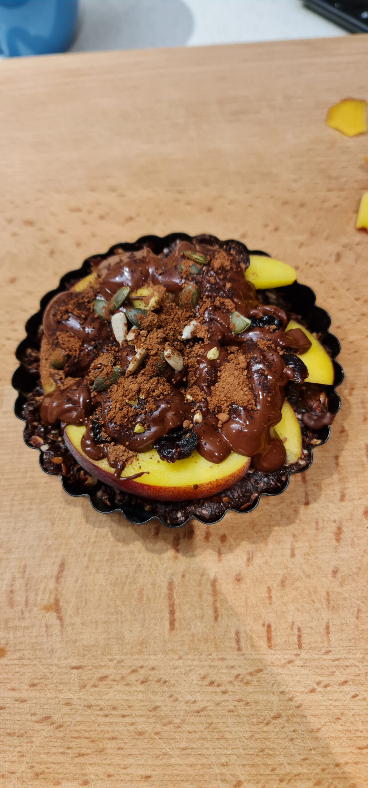 Finished chocolate tart dusted with cocoa, topped with nectarine slices and seeds