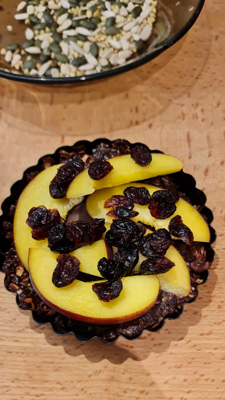 Tart layered with nectarine slices and raisins, bowl of mixed seeds behind