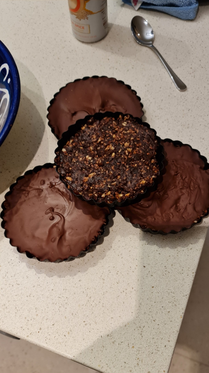 Four tart tins, three sealed with set chocolate and one showing the nut and seed base